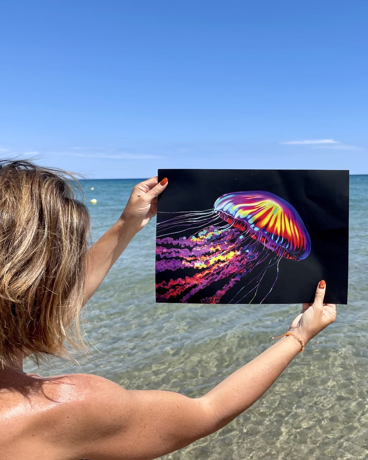 A customer holding up a finished neon jellyfish canvas at the beach